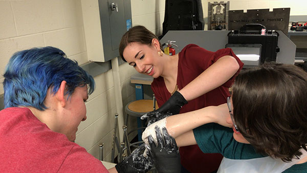 Morgan Sutherland (center) practices applying a mold to a teammate's elbow prior to making a mold of Dylan's stump
